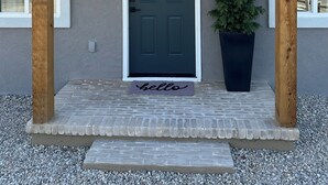 Una casa con una puerta verde oscuro, un felpudo que dice 'hello' y una planta en maceta en el porche.