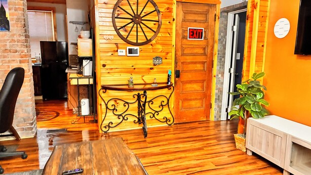 Un interior de madera con un gran adorno de rueda, una silla de oficina negra, una mesa de madera y un televisor montado en la pared.
