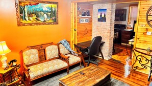 Una sala de estar acogedora con un sofá, una mesa de centro de madera y una lámpara. Hay un cuadro en la pared y un letrero que dice 