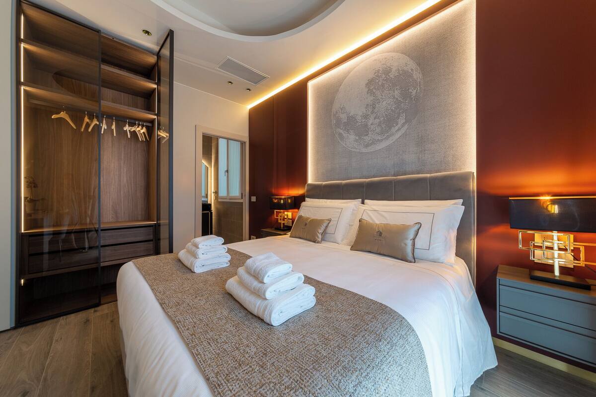 A modern hotel room with a large bed, a walk-in closet, and a wall-mounted artwork.