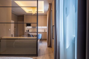A modern hotel room with a sofa, a dining area with a table and chairs, a kitchen area, and a large window with curtains. - MW apartments (Milan)