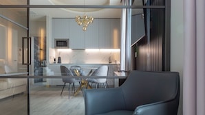 A modern living room with a grey sofa, a dining area with a glass table, and a kitchen with white cabinets and a gold chandelier. - MW apartments (Milan)