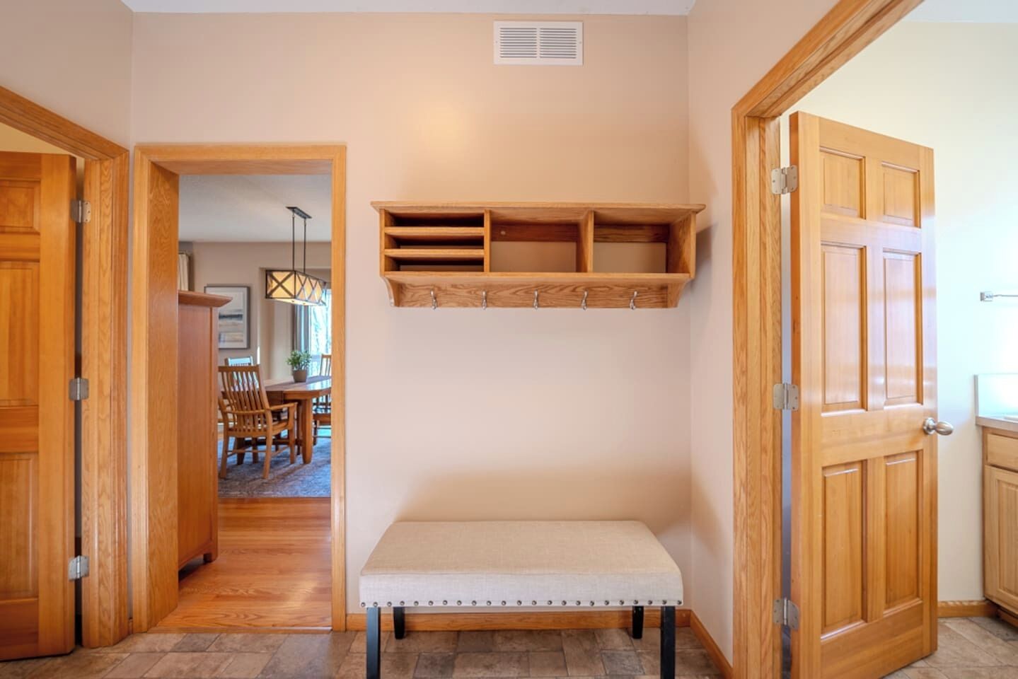 A hallway with wooden doors, a bench, and a wall-mounted shelf unit.