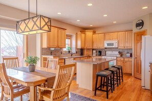 A modern kitchen with wooden cabinets, a central island, bar stools, and a dining area with chairs. - Spacious Modern 5-Bed Home –  Near Twin Cities (Rosemount)