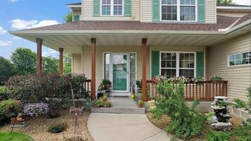 A two-story house with a covered porch, a front door, and a small garden with various plants and flowers.