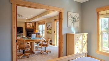 A bedroom with a bed, a desk with chairs, a dresser, and a painting on the wall.