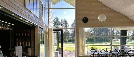 Ein Restaurant mit Barbereich, Außenbereich und großen Fenstern mit Blick auf einen Golfplatz.