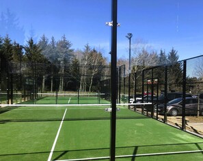 Een tennisbaan met een net, omheind door een hek, en bomen op de achtergrond.