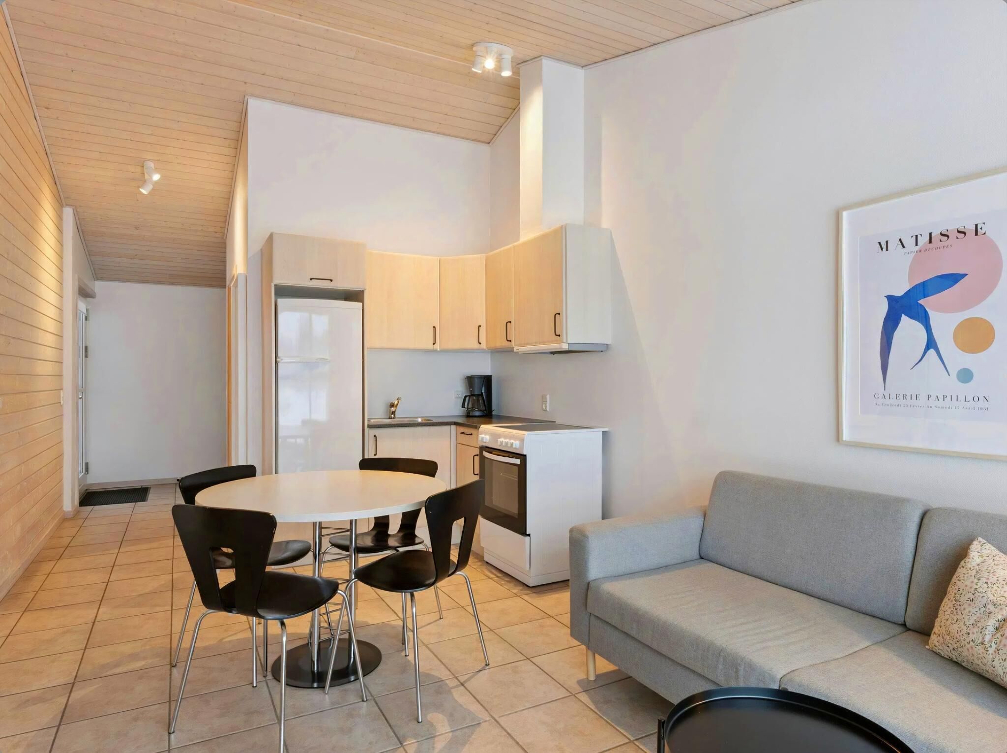 A modern kitchen with white cabinets, a dining table with chairs, a gray sofa, and a framed artwork on the wall.
