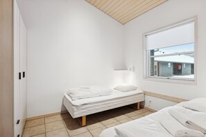 A small, clean room with a single bed, a window with a view of a building, and a wooden ceiling. - Holiday apartment near beach and golf (Pandrup)