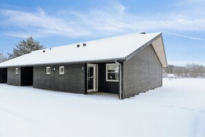 A large, single-story building with a sloped roof, multiple garage doors, and a door leading to a covered entrance. - Holiday apartment near beach and golf (Pandrup)