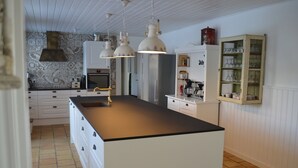 Een keuken met een centraal eiland, hanglampen, witte kastjes en een decoratieve spatwand.