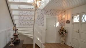 Een trap met witte leuningen, een houten tafel met een lamp, een vaas met bloemen en een deur met een decoratief glasraam.