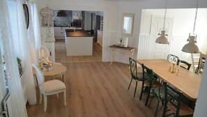 Een eetruimte met een houten tafel en stoelen, een keuken op de achtergrond en een witte deur.
