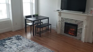A living room with a fireplace, a TV, and a dining area with a table and chairs. - Cozy Harlem Brownstone 1BR Washer & Dryer (New York)