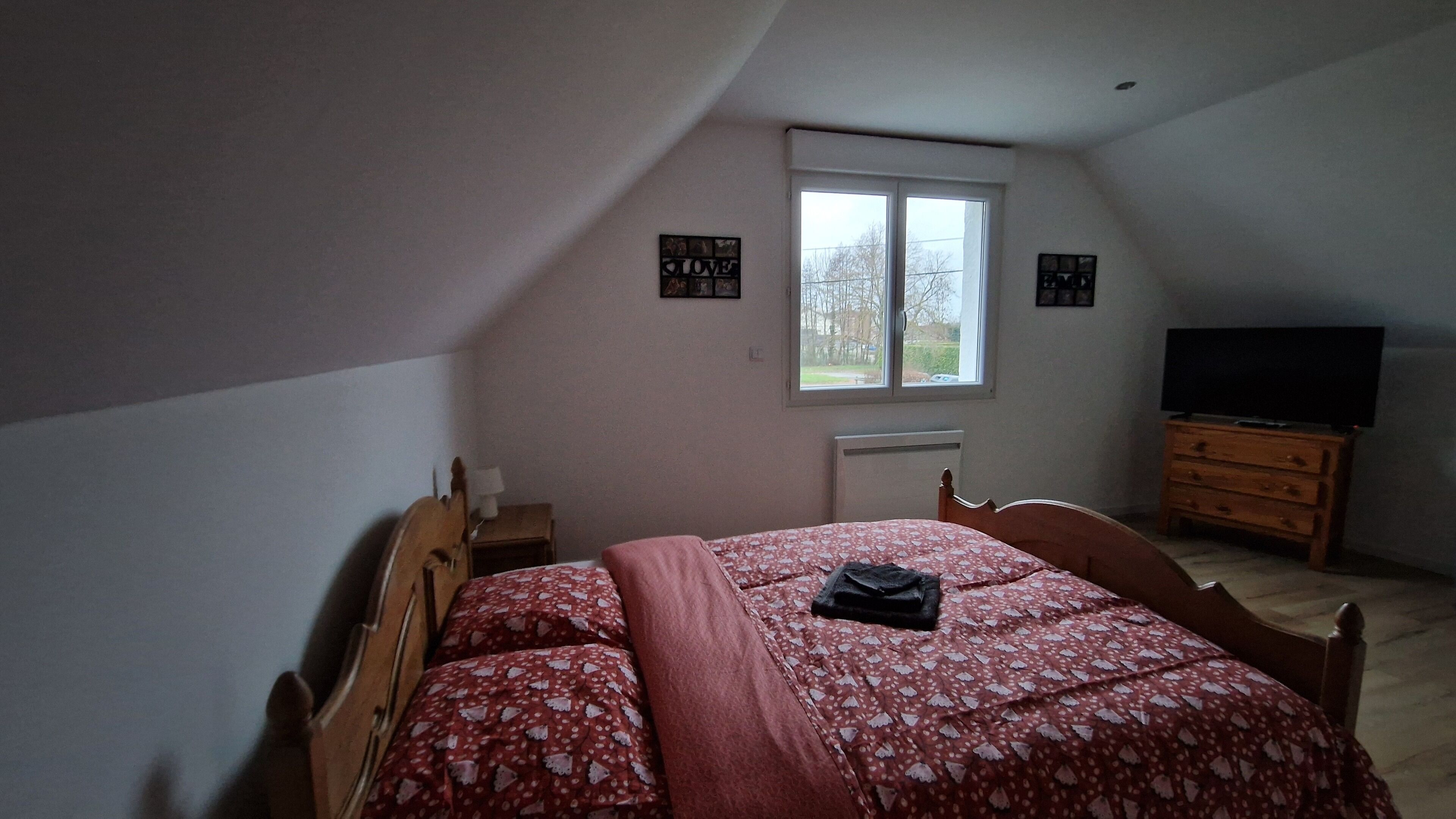 Ett sovrum med ett sluttande tak, en säng med ett blommigt överkast, en byrå, en tv och ett fönster med utsikt över träd.