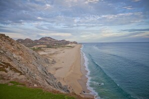 Paisaje costero con una playa arenosa, acantilados rocosos y vistas al océano.