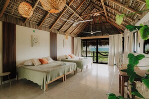Een kamer met twee bedden, een plafondventilator en uitzicht op de oceaan.