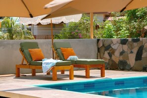 Zwei Holzliegen mit Kissen, eine Steinmauer und ein Pool.