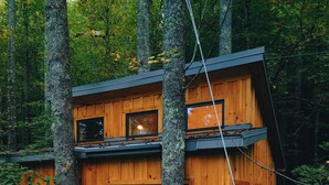 A wooden cabin with a balcony, surrounded by trees.