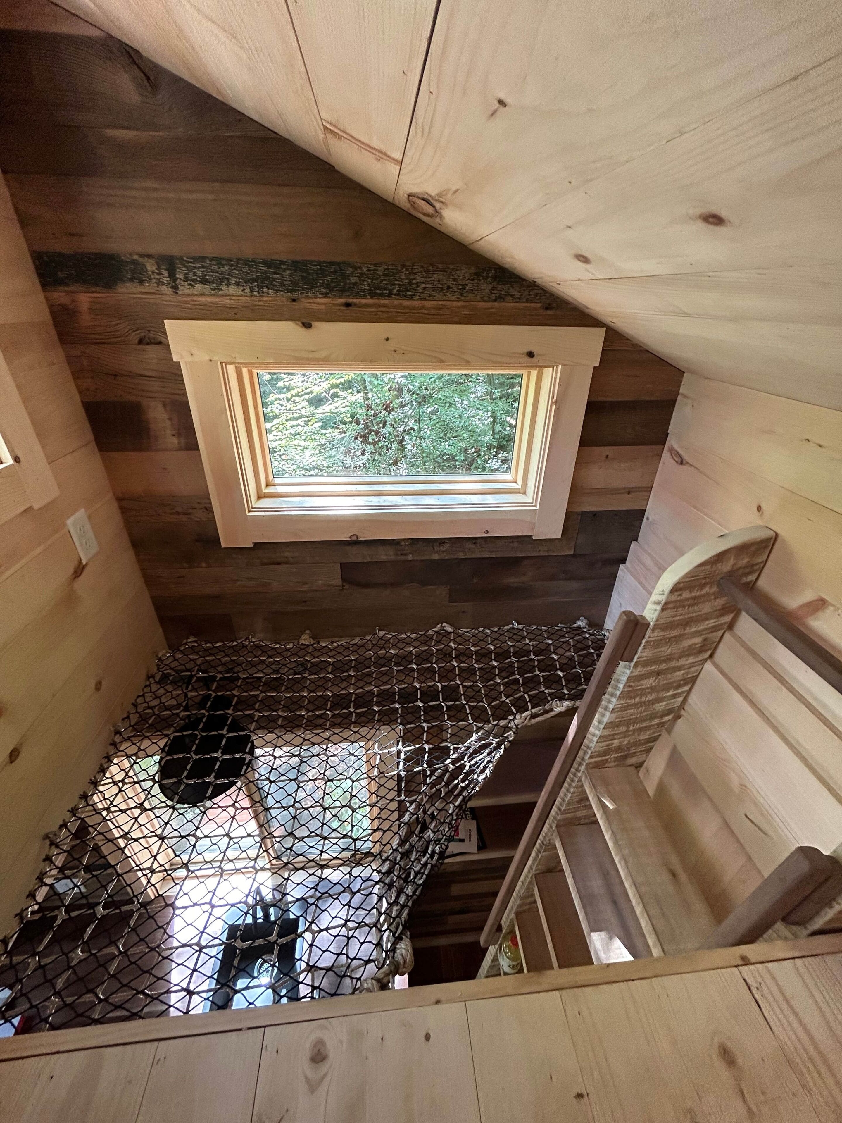 Une cabane en bois avec une chambre à coucher située en mezzanine, un puits de lumière et un plancher en treillis métallique.