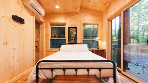 A wooden cabin bedroom with a bed, a small table, and a window.