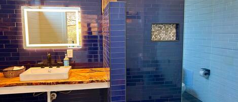 A bathroom with a dark blue tiled wall, a white sink with a mirror, and a glass shower enclosure.