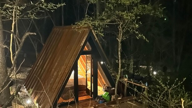 Une petite cabane rustique avec un toit en pente, une terrasse en bois et une seule fenêtre visible.