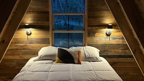 Une chambre à coucher avec un grand lit, une fenêtre donnant sur les arbres et deux lampes fixées au mur.