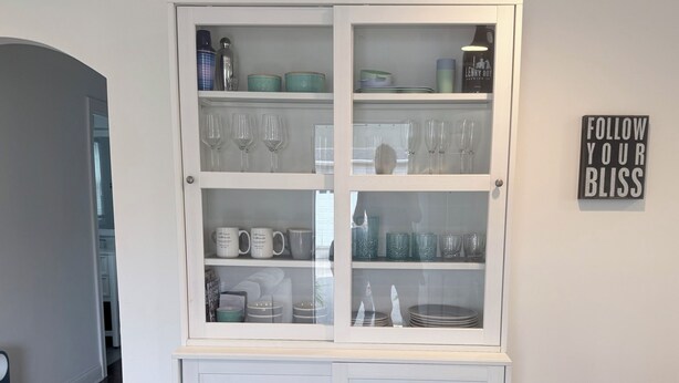 A white cabinet with glass doors containing various kitchenware and glassware.