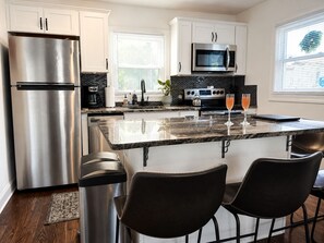 A modern kitchen with stainless steel appliances, a granite countertop, and a bar area with two chairs.