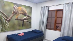 A room with two single beds, a large wall mural of a monkey, a window with curtains, and a small table with a towel. - Hermoso y cómodo apartamento en Leticia No 1 (Leticia)