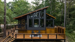 A cabin with a deck, large windows, and a fire pit.