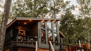 A cabin with a wooden exterior, a staircase leading to a deck, and a view of the surrounding forest.
