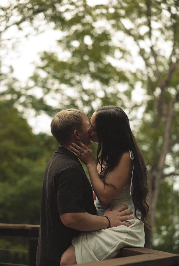Una pareja abrazándose al aire libre, con árboles al fondo.