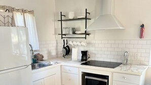Una cocina compacta con armarios blancos, horno integrado, lavamanos y un tendedero colgante sobre la encimera.