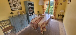 Ein Zimmer mit Esstisch, Stühlen, einem Schrank und einem Fenster mit Vorhängen.
