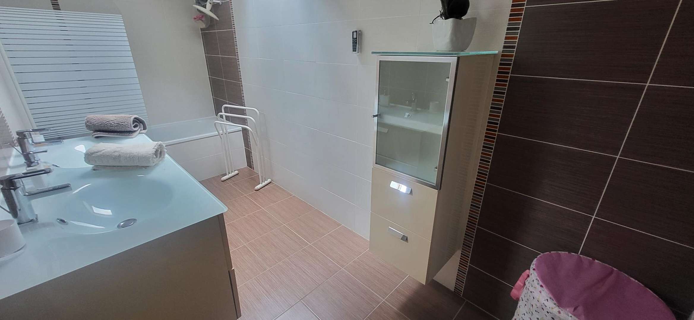 Een badkamer met een wastafel, spiegel, handdoek, douche en een glazen kastje.