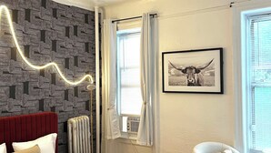 Une chambre à coucher comprenant un lit, un radiateur, une chaise, une fenêtre avec des rideaux, un tableau accroché au mur et un luminaire au plafond.