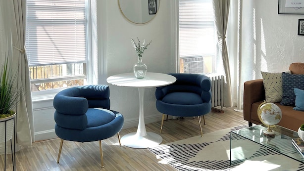 Un salon moderne avec une table ronde blanche, deux fauteuils bleus, un canapé marron et un globe posé sur une table basse en verre.