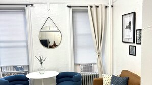Un salon moderne avec un canapé marron, des fauteuils bleus, une table basse blanche et un miroir rond accroché au mur.