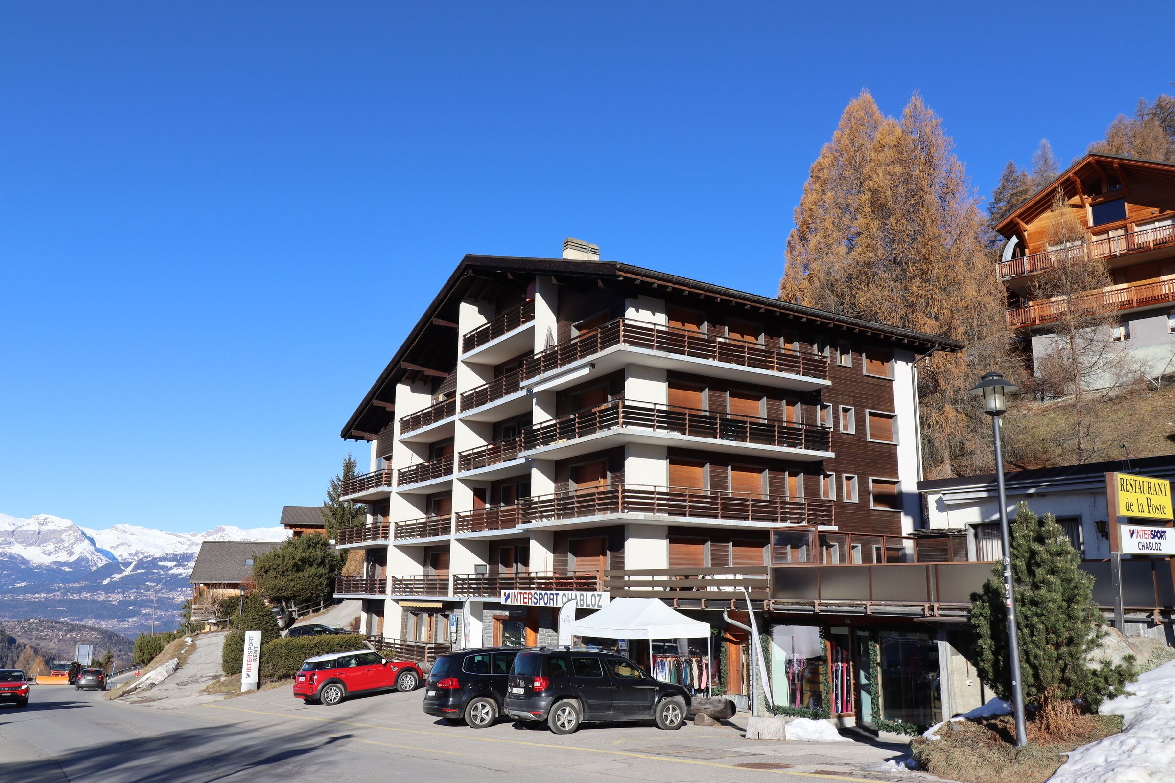 Ein mehrstöckiges Hotel mit Balkonen, einem Restaurant und einem Skigebiet im Hintergrund.