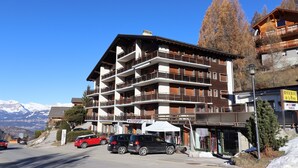 A multi-story hotel with balconies, a restaurant, and a ski resort in the background.