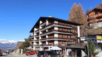 Ein mehrstöckiges Hotel mit Balkonen, einem Restaurant und einem Skigebiet im Hintergrund.