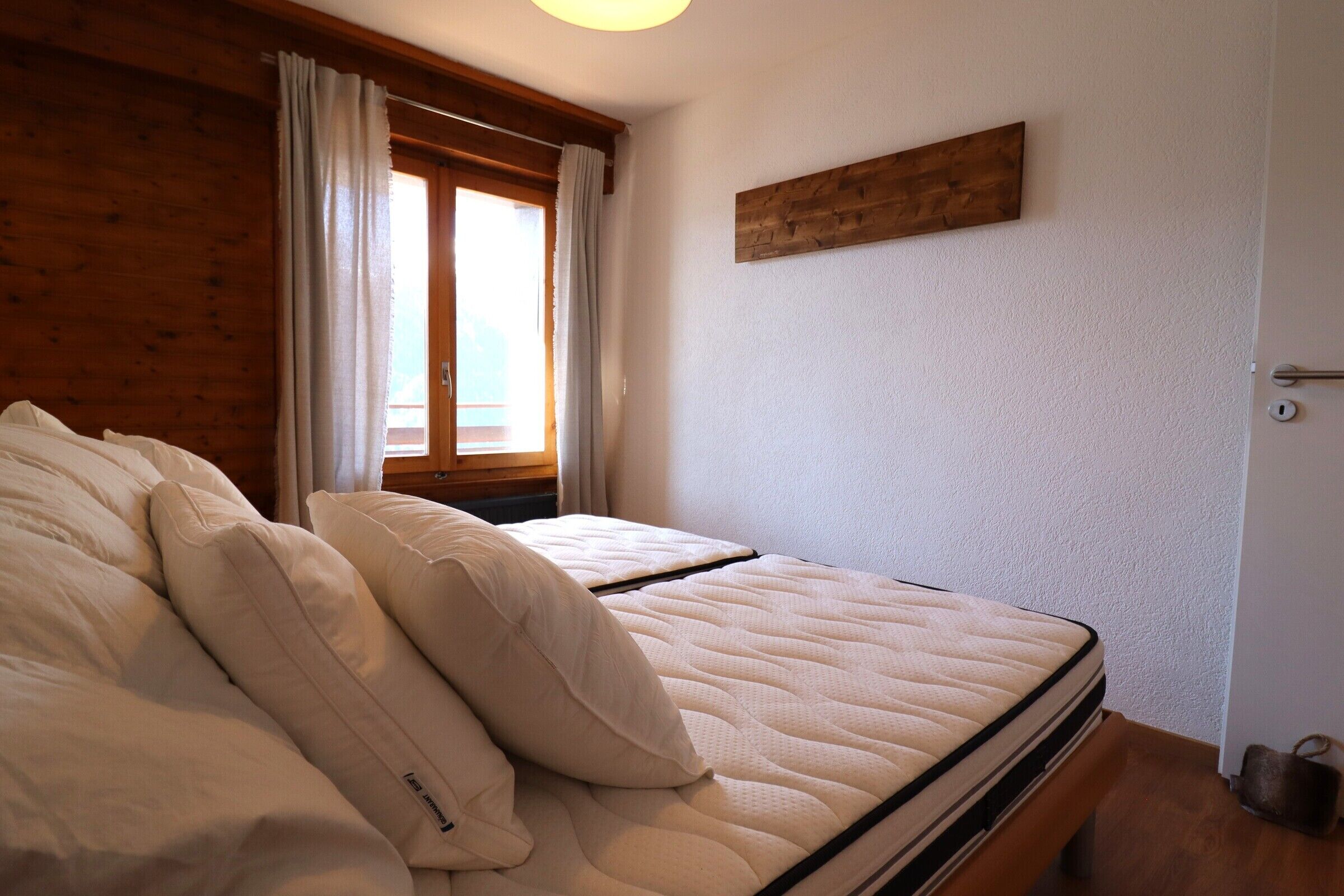 Ein Schlafzimmer mit Bett, Holzwänden, einem Fenster mit Vorhängen und einem hölzernen Kopfteil.