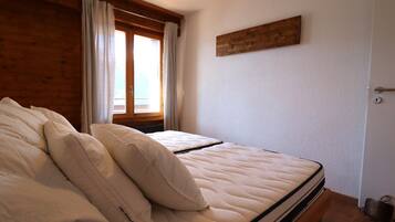 Ein Schlafzimmer mit Bett, Holzwänden, einem Fenster mit Vorhängen und einem hölzernen Kopfteil.