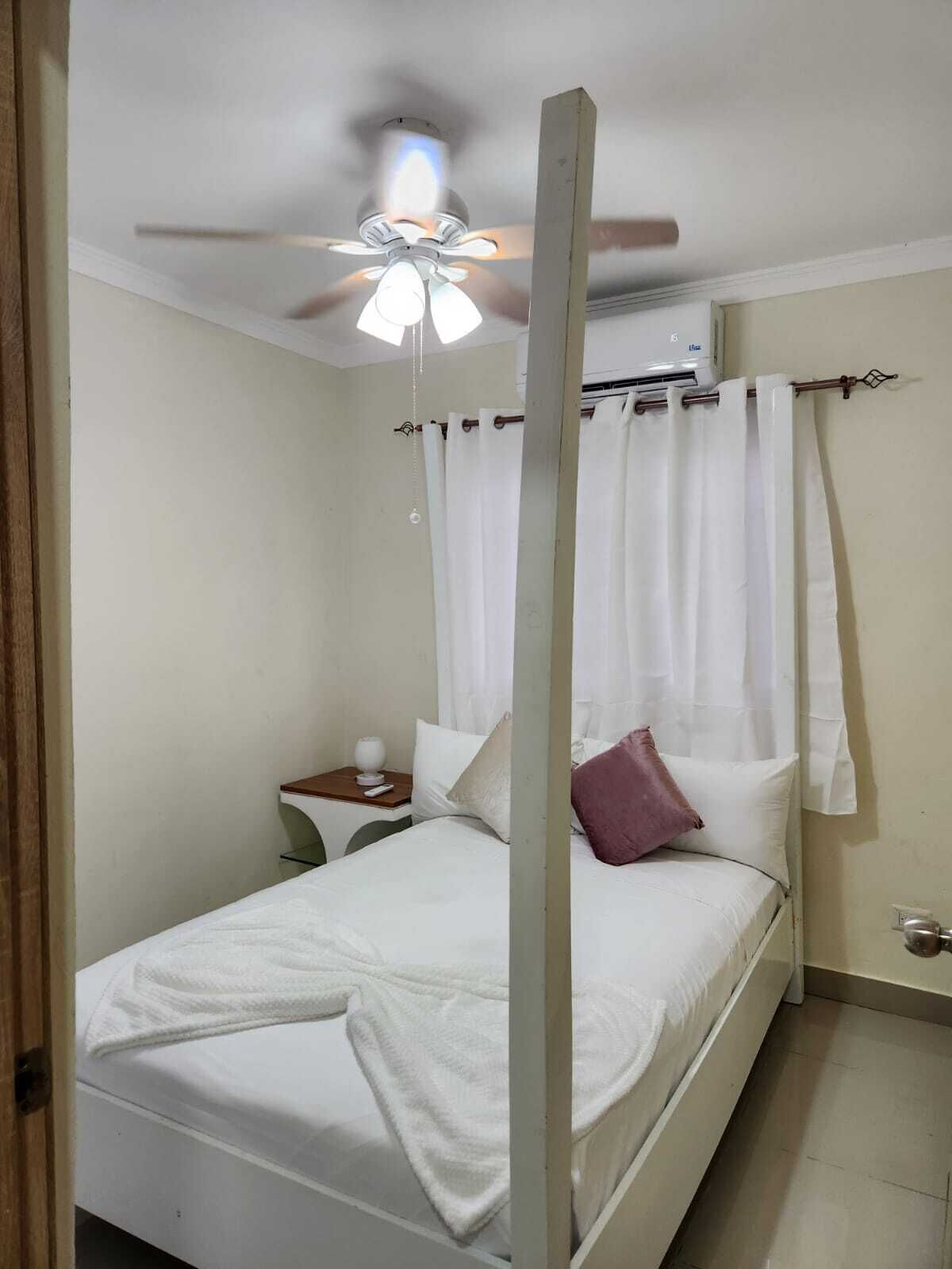 A single bed with a canopy, a bedside table with a lamp, and a ceiling fan.