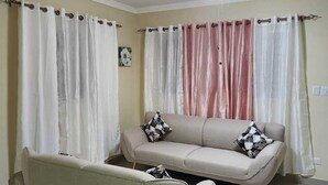 Ein Wohnzimmer mit Sofa, Sessel, Deckenventilator und Vorhängen.