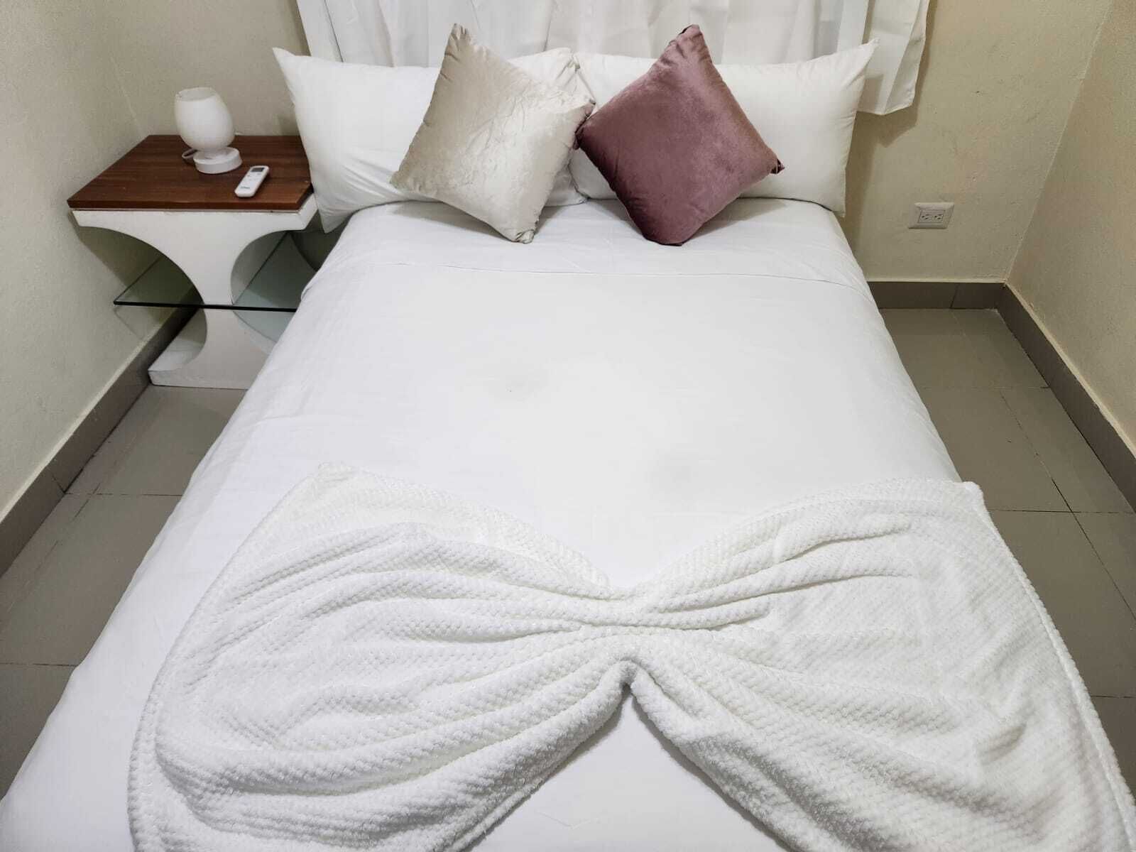 A neatly made bed with white bedding, a white throw blanket, and two pillows, one white and one pink.