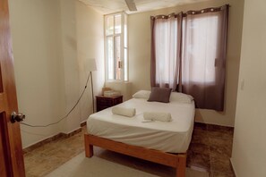 A bedroom with a wooden bed, a bedside table, a lamp, and a window with curtains. - Private 1BR - Pool- AC- La Punta - Private Kitchen & Bath (brisas de zicatela)
